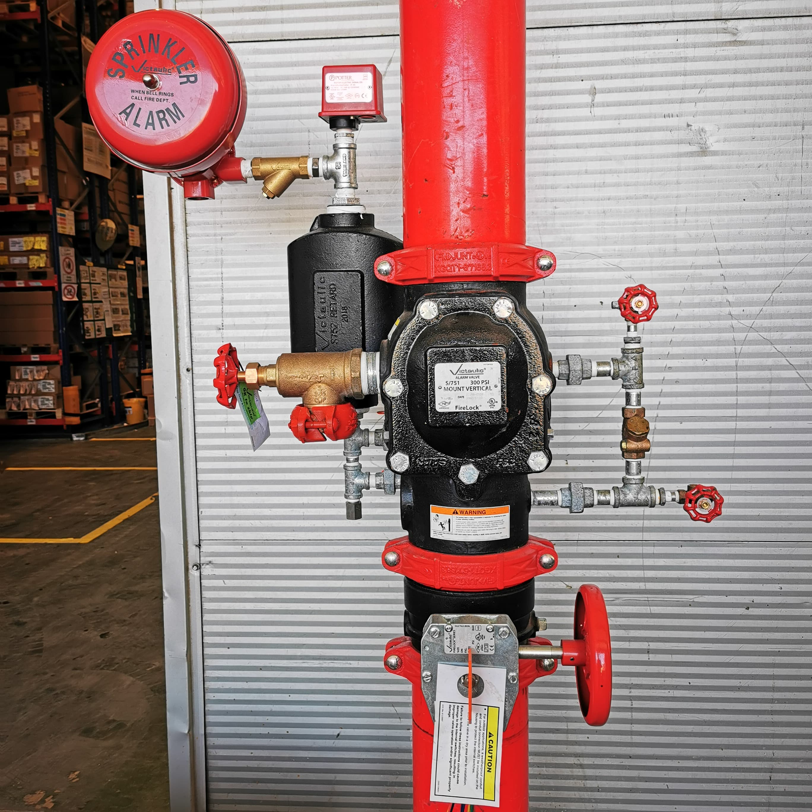 Vanne d'alarme de gicleur d'incendie rouge et noire avec cloche d'alarme dans un entrepôt.