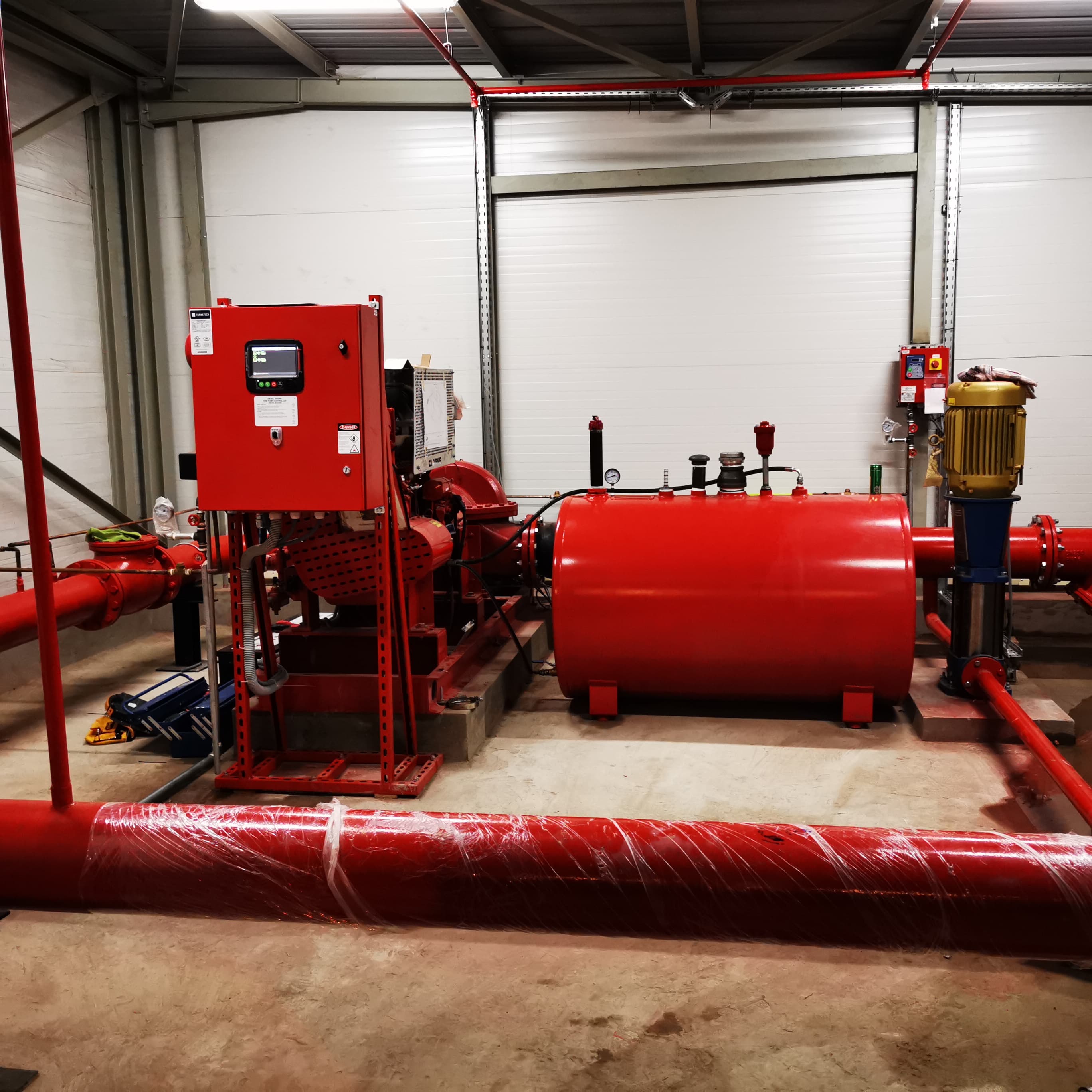 Système de pompe à incendie rouge avec réservoir et tuyauterie dans un bâtiment industriel.