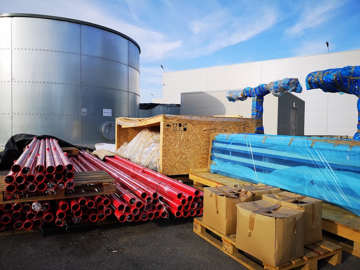 Grand réservoir métallique, tuyaux rouges empilés et matériel de construction sur un site industriel.