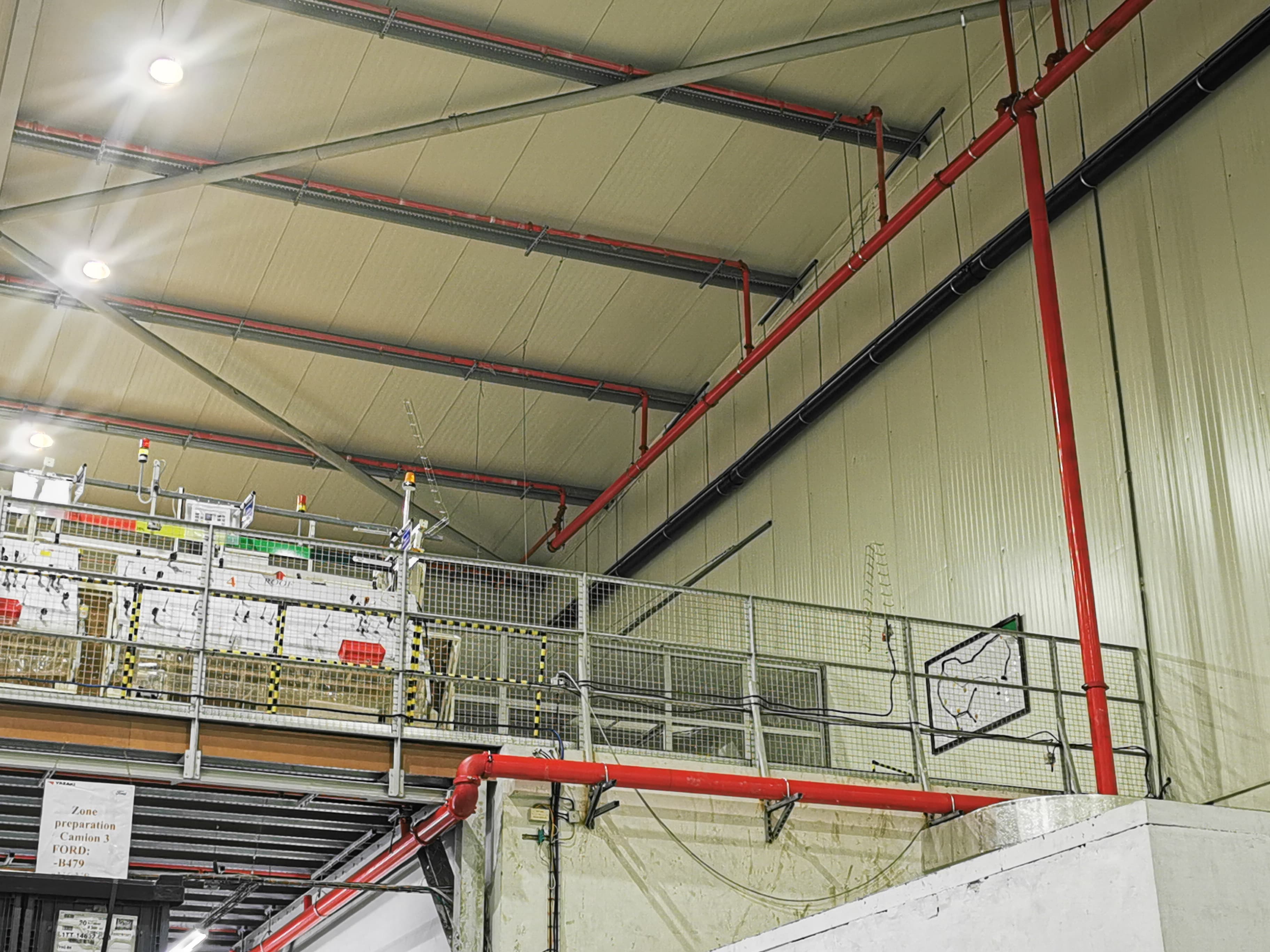 Intérieur d'un entrepôt industriel avec des tuyaux d'incendie rouges et une mezzanine de sécurité.